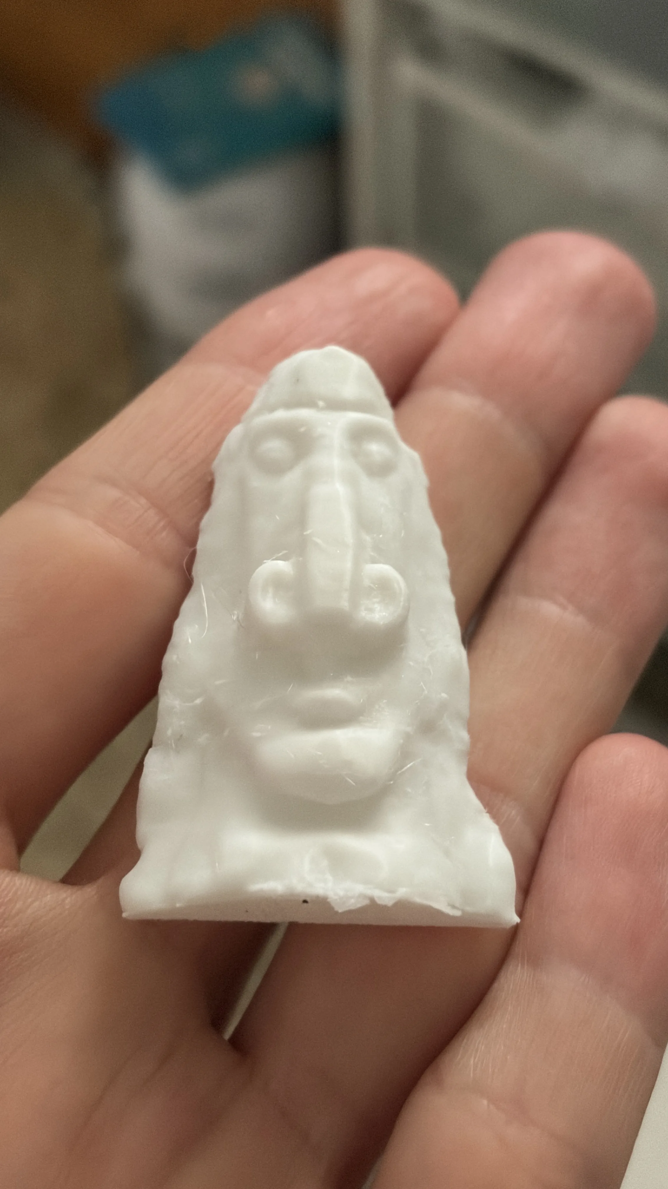 A white 3D printed statue of a desert rock shaped like a face, held in a hand
