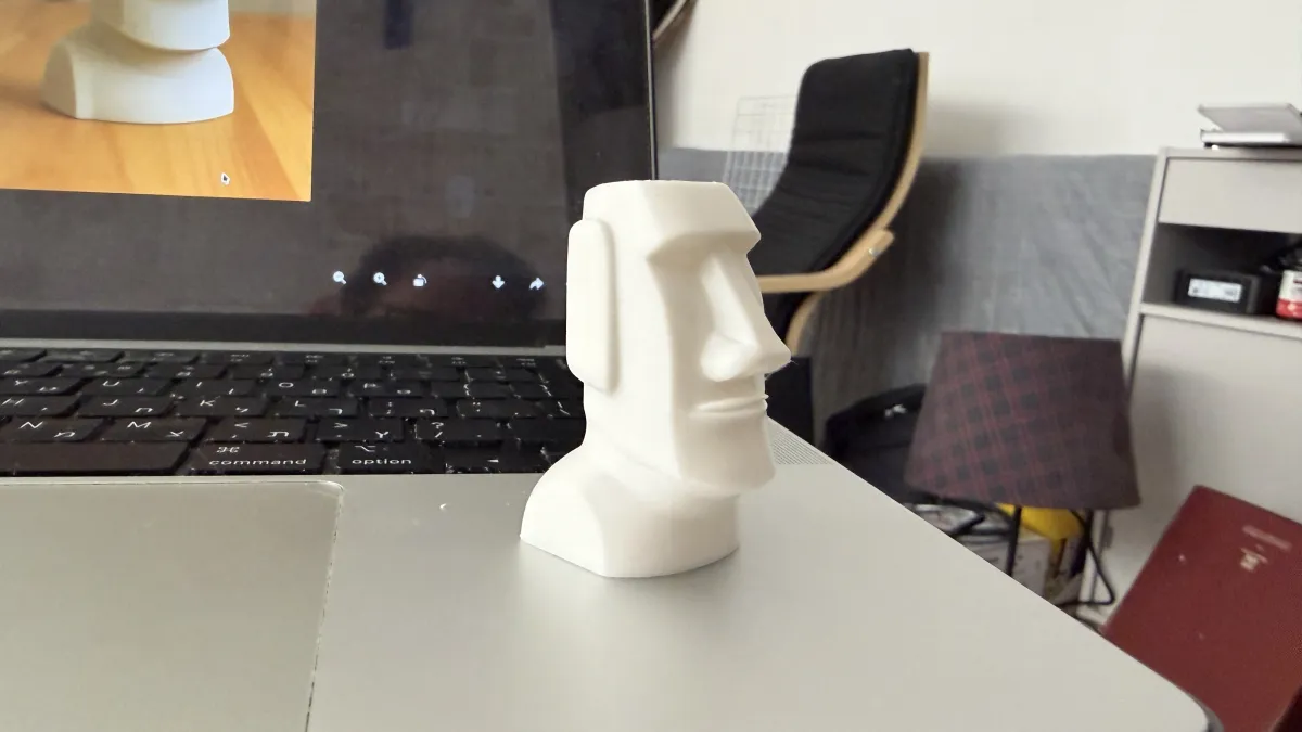 The 3D printed moai on a desk beside the laptop that generated it